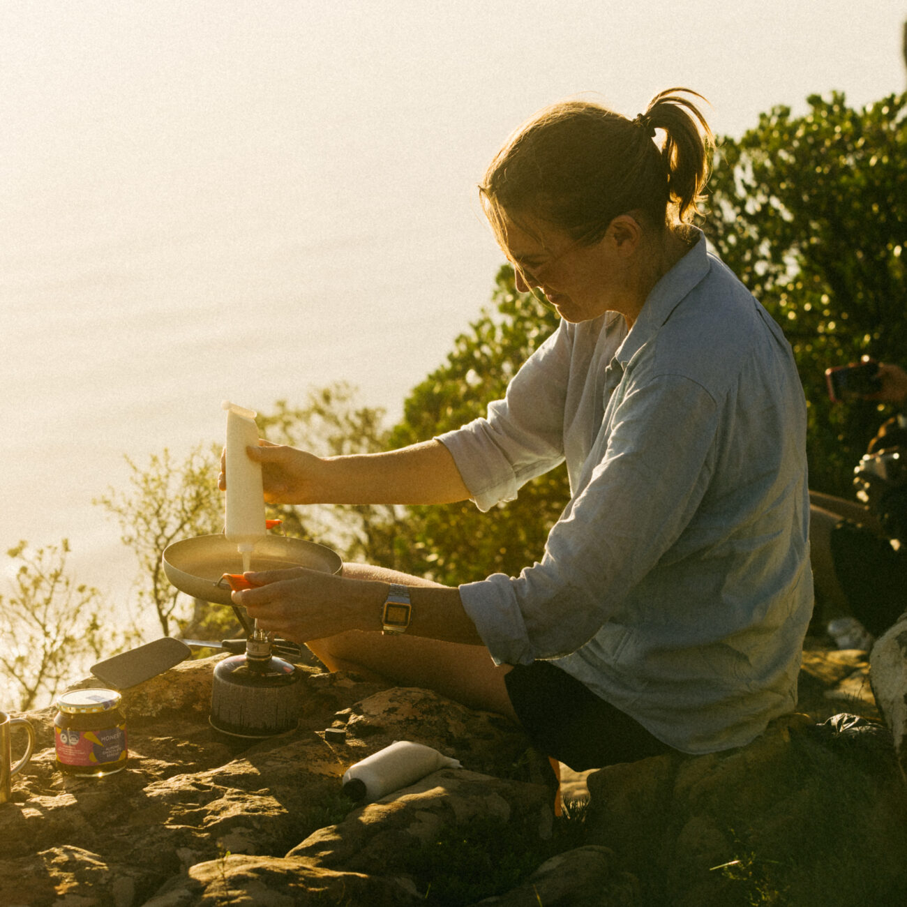 female hiker making pancakes on top of mountain