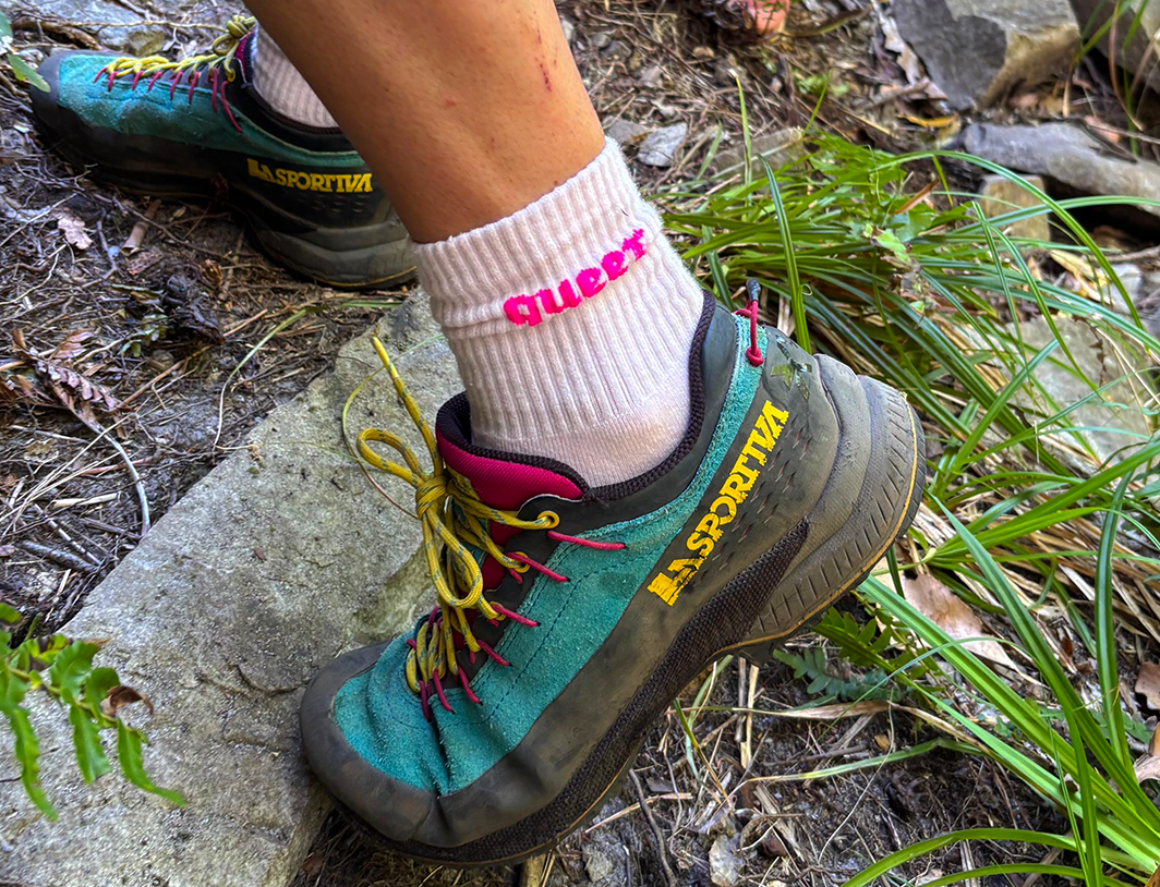woman with hiking shoe and sock that says "queer"