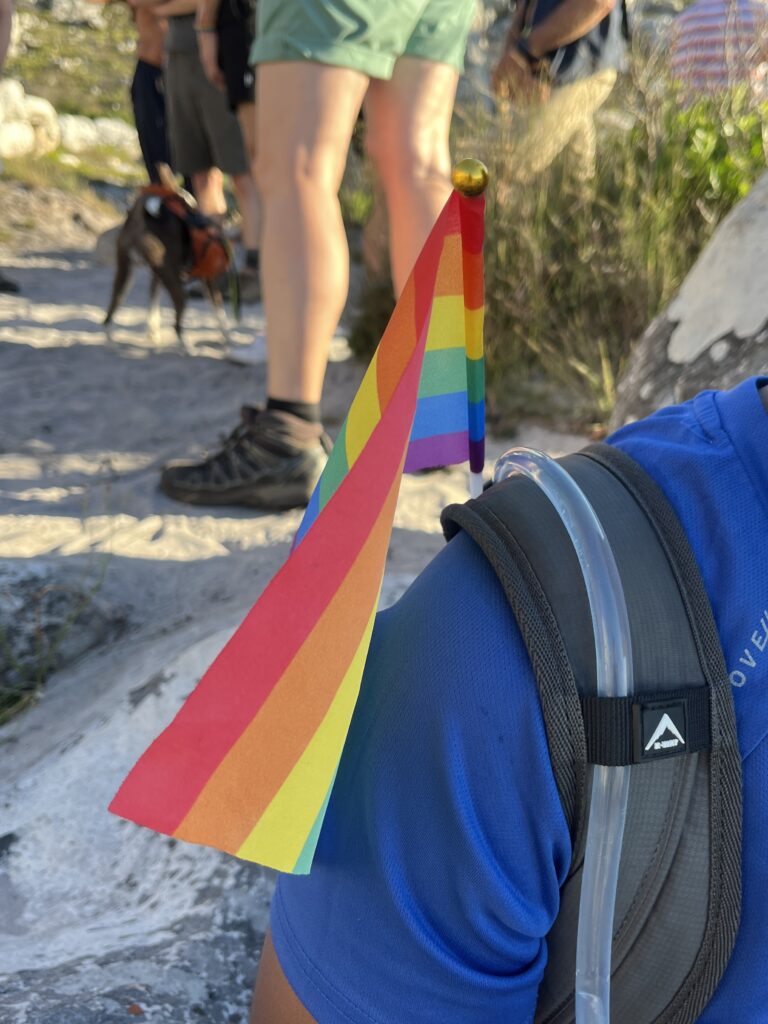 hiker on mountain with pride flag on backpack